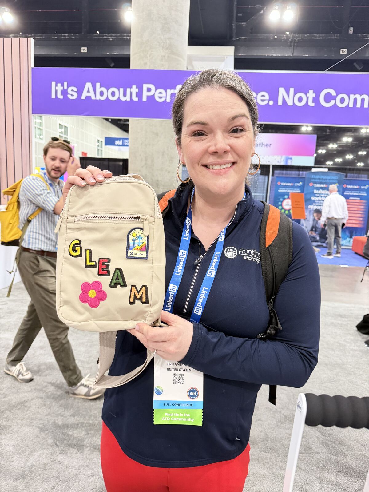 Person displaying an embroidered tote bag with decorative patches at an indoor event booth